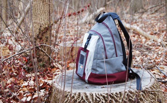 A backpack prototype sits on a stump in the woods
