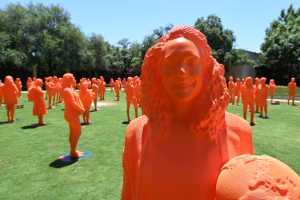Life-sized orange 3D-printed statues of women stand on a lawn