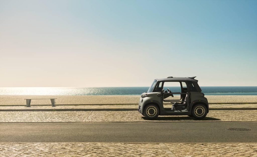 A tiny electric vehicle sits on a beach with the ocean behind